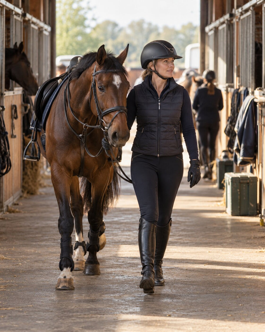 Riding instructor leading the next saddled horse down the stable aisle